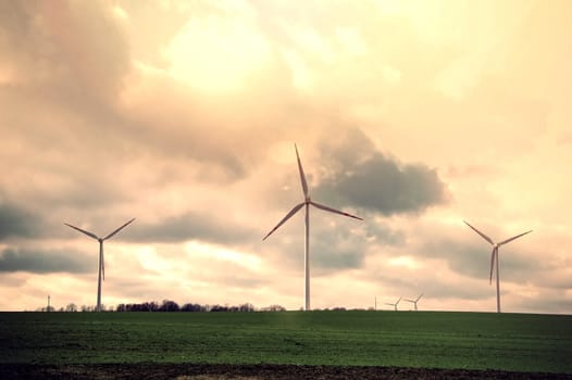 Windmills on the green field against dark cloudy sky. Alternative energy.