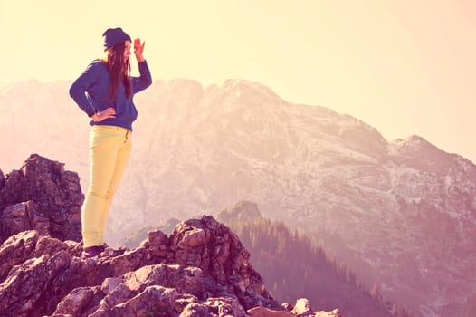 Young beautiful girl standing on the rocks in mountains and looking for new opportunities. Vintage instagram picture.