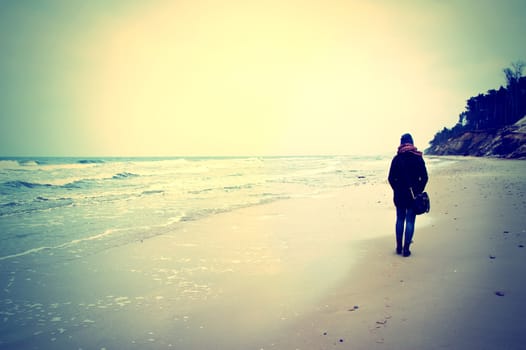 Emotion conceptual image. Lonely woman walking on the beach. Instagram vintage picture.