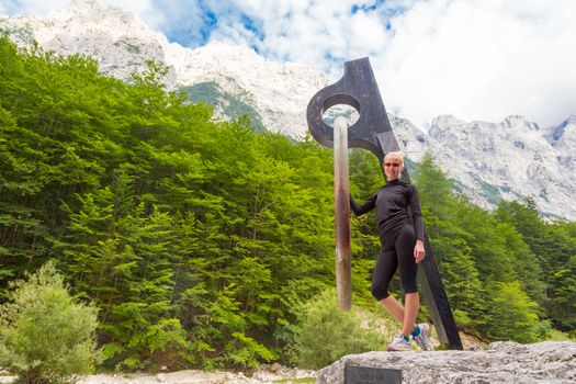 Active sporty woman relaxing in beautiful natural mountain environment by statue of mighty piton, monument to victims of mountains in Vrata Valley in Triglav National Park in Julian Alps, Slovenia.