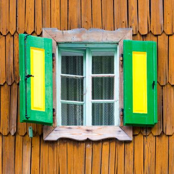Decorative, green yellow, vintage, window shutters on a brown wooden wall. Retro detail from traditional alpine mountain house with wooden paneling. Austria, Germany, Slovenia. Square composition.