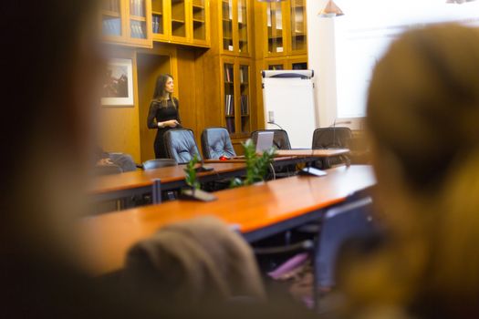 Speaker giving presentation in lecture hall at university. Female PhD candidate defending her doctoral thesis in front of the committee. Participants listening to presentation.