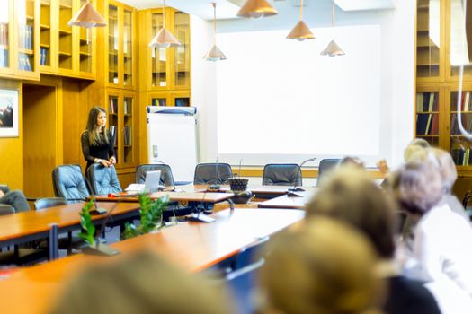 Speaker giving presentation in lecture hall at university. Female PhD candidate defending her doctoral thesis in front of the committee. Participants listening to presentation.