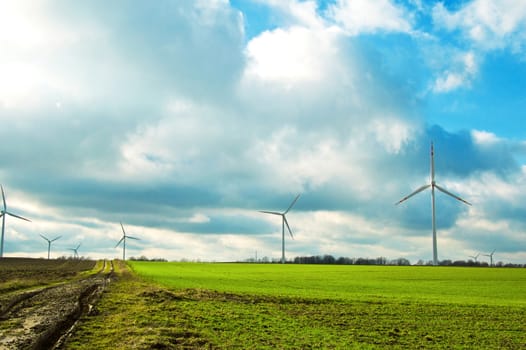 Windmills on the green field against cloudy sky. Alternative energy