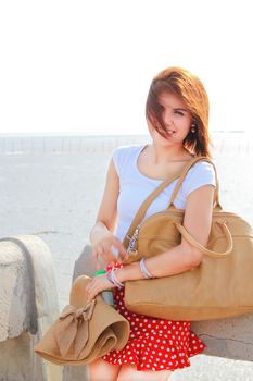 Happy lady at the beach with her brown hat and leather bag