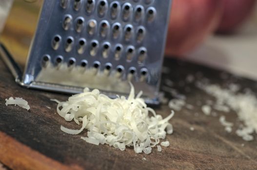 Grated cheese and grater on cutting board close up