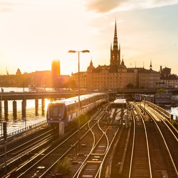 Railway tracks and trains near Stockholm's main train station in Norrmalm area, Stockholm, Sweden in sunset.  Silhouette of city hall and cathedral in background. Square composition.