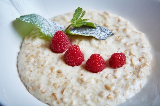 oatmeal with raspberries and mint in white plate
