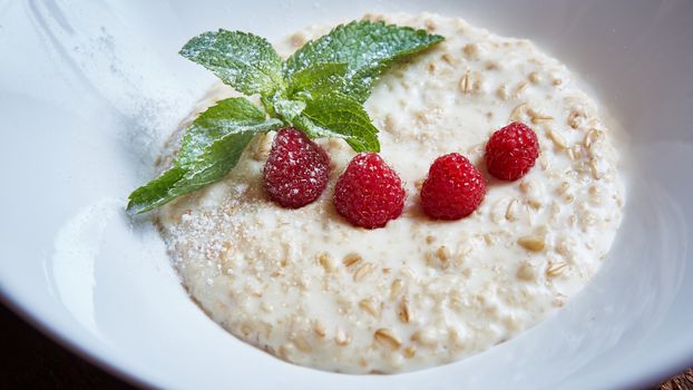 oatmeal with raspberries and mint in white plate