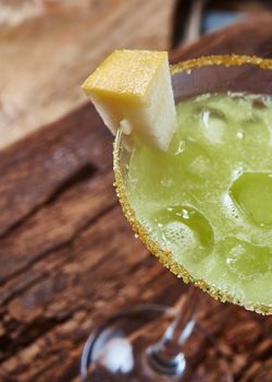 Green margarita melon cocktail with copy space on wooden background.