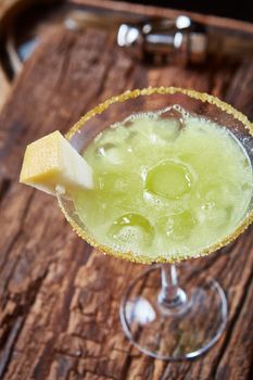 Green margarita melon cocktail with copy space on wooden background.