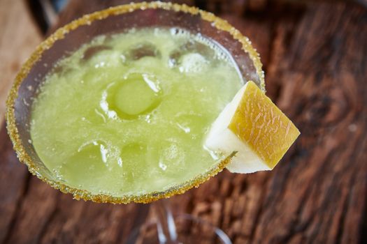 Green margarita melon cocktail with copy space on wooden background.