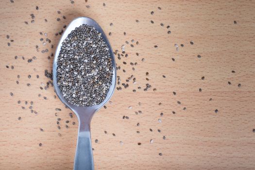 Chia seeds in stainless steel spoon on wooden texture