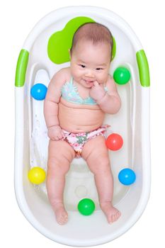 Asian baby girl in bikini taking a bath and put finger in her mouth. play in the white tub and have many color balls