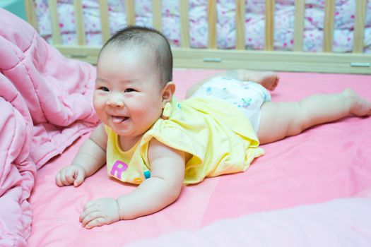 Asian baby girl smile and tongue out on pink bed, weared yellow shirt and diaper