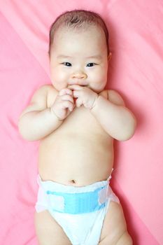 Asian baby girl weared diaper on pink bed , smile and looking at the camera.