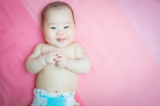 Asian baby girl weared diaper smile and tongue out. She lay on pink bed and looking at the camera.