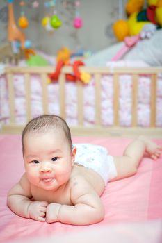 Asian baby girl scowl and tongue out, she overturn on pink bed whit her toys in blackground