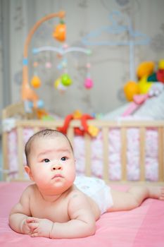 Asian baby girl scowl and tongue out, she overturn on pink bed whit her toys in blackground