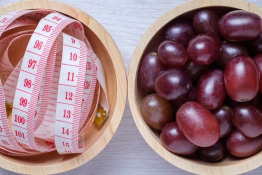 Red grapes and tape measure in wooden bowl. they on white wooden table. Clear light. this photo use for descript weight loss, diet, eat clean