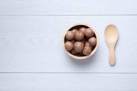 Macadamia in wooden bowl near wooden spoon on white wooden table