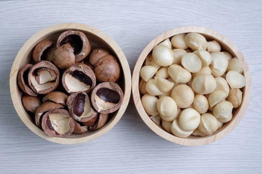 Macadamia nuts and shells in wooden bowl put on white wooden table