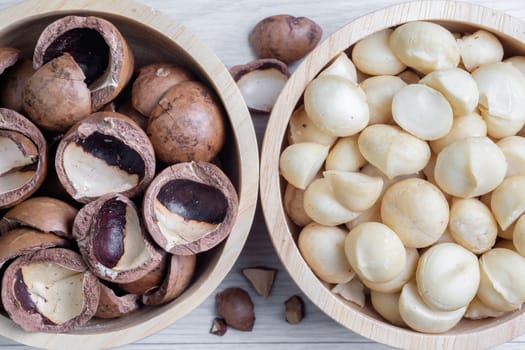 Macadamia nuts and shells in wooden bowl put on white wooden table