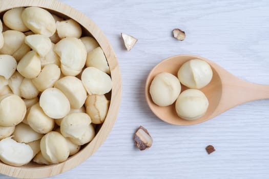 Macadamia nuts and shells in wooden bowl put on white wooden table