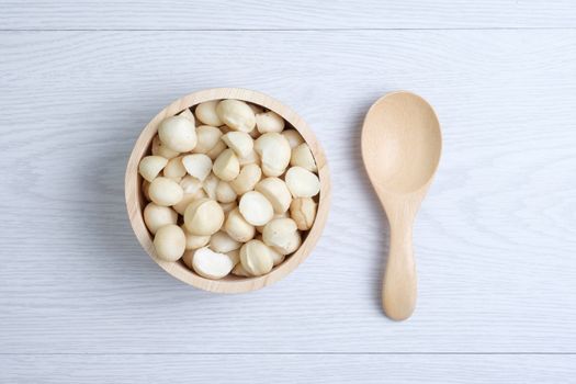 Macadamia nuts and shells in wooden bowl put on white wooden table