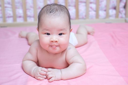 Asian baby girl lie prone on pink bed and looking at the camera
