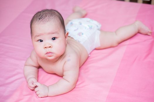 Asian baby girl scowl on pink bed and she looking at the camera
