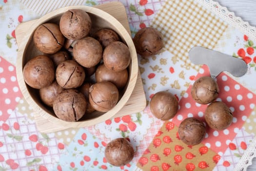 Macadamia on napery and wooden bowl, it waiting for unshell with macadamia opener