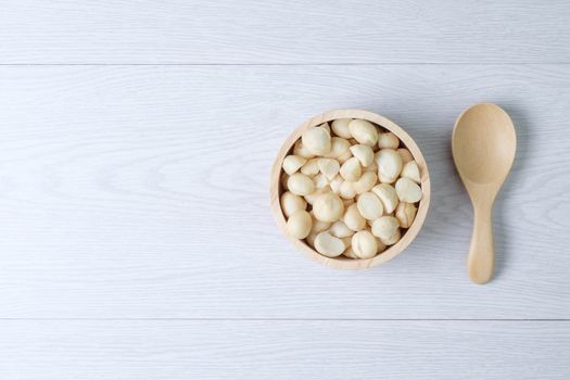 Macadamia nuts and shells in wooden bowl put on white wooden table