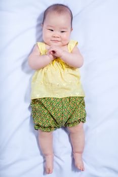 top-view asian baby girl in traditional thai dress, she lie down, smile , touching her hands and looking at camera