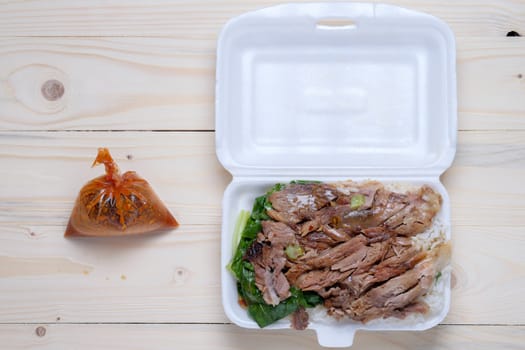 Stewed Pork Leg with Rice in foam box and suace in plastic bag on wooden table