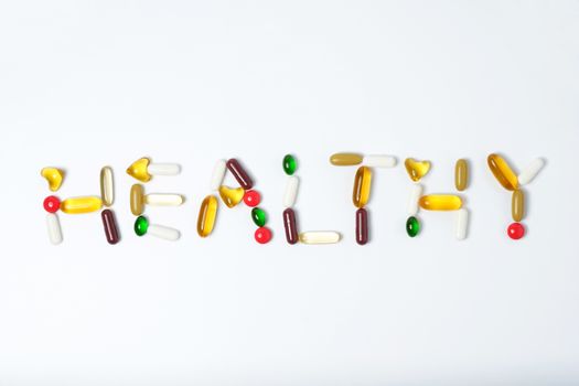 Healthy words made by pills of vitamin and medicine on white background