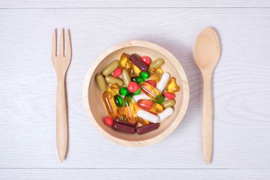medicine and vitamin on wooden bowl with wooden spoon and fork