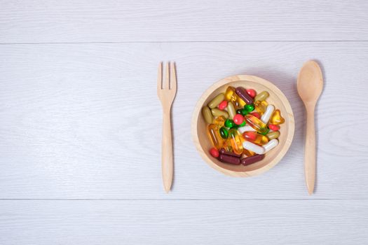 medicine and vitamin on wooden bowl with wooden spoon and fork