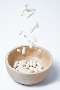 falling of white capsules medicine or vitamin in to wooden bowl