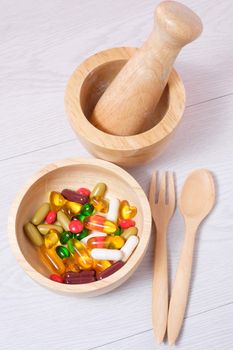 medicine and vitamin on wooden bowl with wooden spoon, fork and mortar