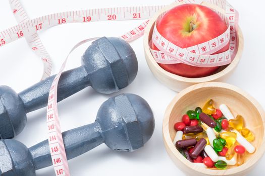 red apple and vitamin (medicine) in wooden bowl with waist measure and dumbbell
 on white background