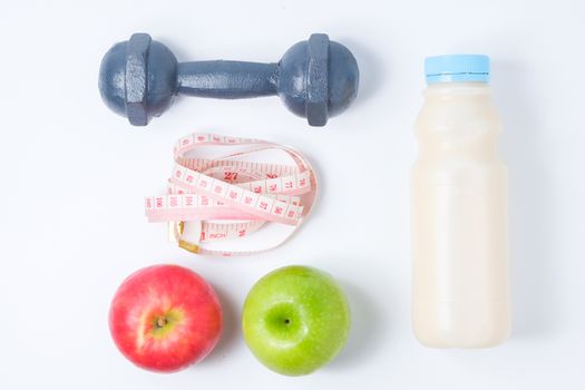 slice red , green apple with dumbbell, waist measure and milk on white background
