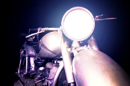 Old vintage motorcycle with turn on light ready to ride into dark night. Transportation conceptual image.