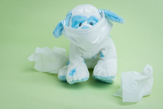 A white and blue stuffed dog wearing a surgical mask surrounded by used tissues representing the idiomatic phrase "sick as a dog."