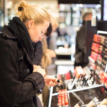 Beautiful blond lady testing  and buying cosmetics in a beauty store.