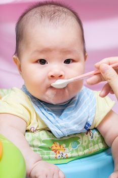 Mother feeding her asian thai baby girl a milk with spoon
