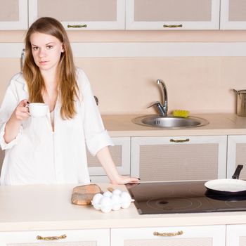 Girl in man's shirt drinking tea standing over the stove