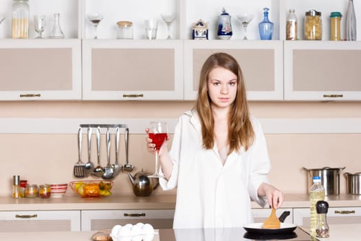 Girl with long flowing hair in a man's shirt in the kitchen with a glass of red wine