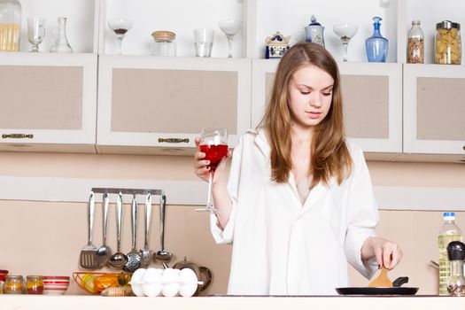 girl in a white men's shirt with a glass of red wine near the pans