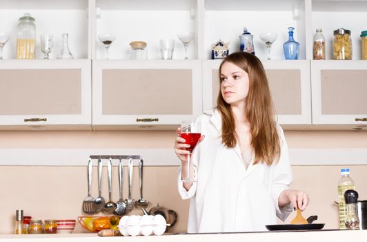 Girl with long flowing hair in a man's shirt in the kitchen with a glass of red wine